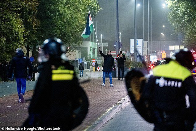 A protester with a Palestinian flag and Mobile Unit (ME) during a pro-Palestinian demonstration during Ajax - Maccabi Tel-Aviv at Anton de Komplein