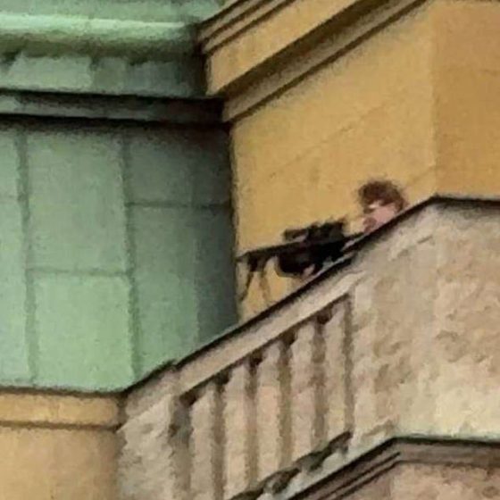 A chilling image shows Kozak dressed in black aiming a rifle at people below while standing on top of a faculty building
