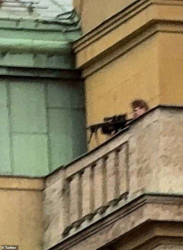 A chilling image shows Kozak dressed in black aiming a rifle at people below while standing on top of a faculty building