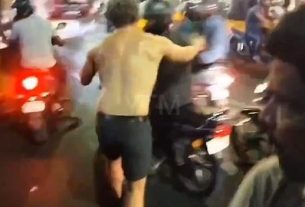 This is the moment a semi-naked man launches himself at a passing motorcyclist before appearing to bite him